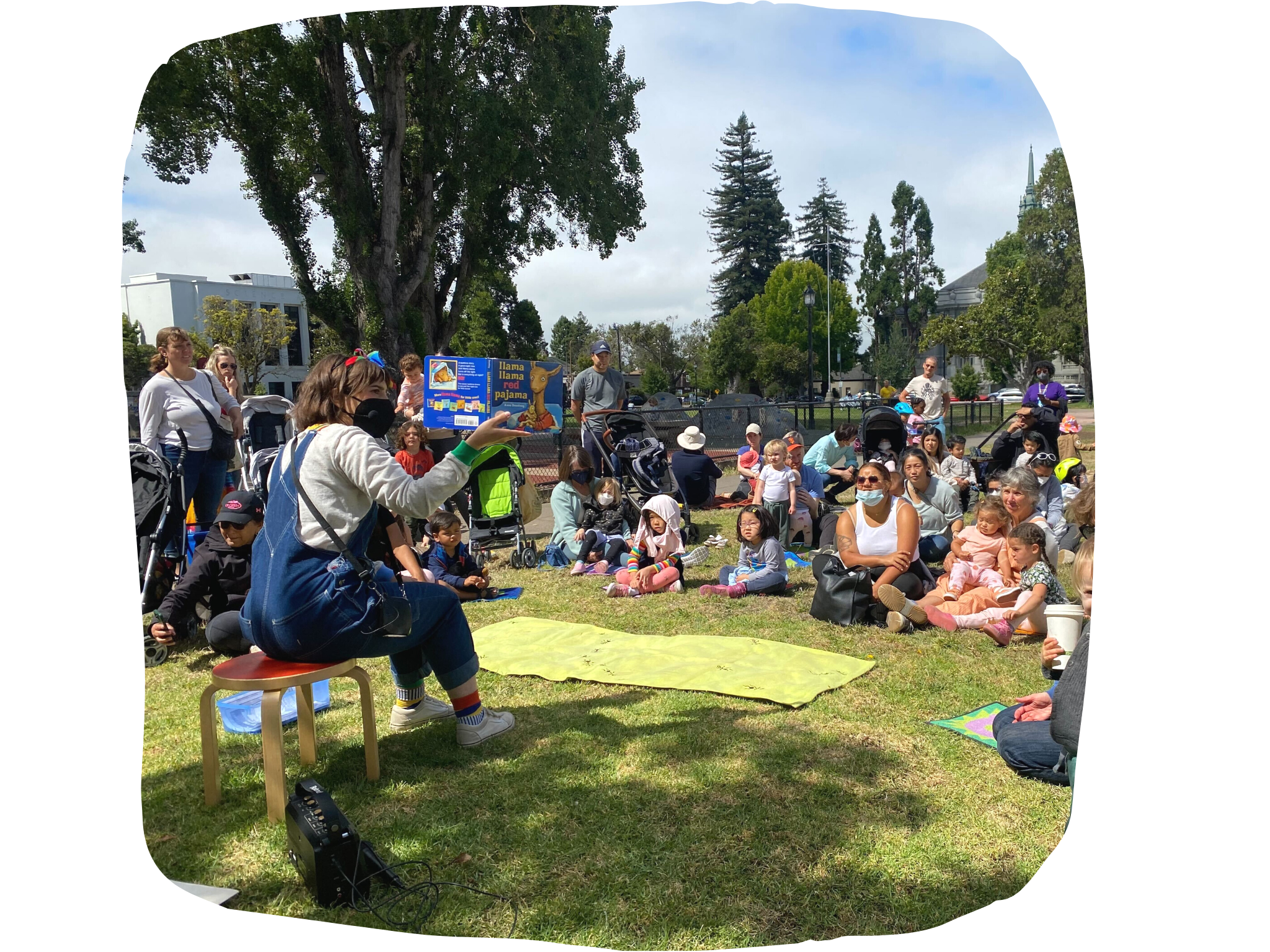 BACT partner Bri Reads sits on the grass and reads to a crowd of families at the Berkeley Farmer's Market