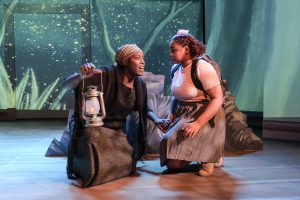 Two actors kneeling down. One is dressed like Harriet Tubman, the other is dressed as a young girl .