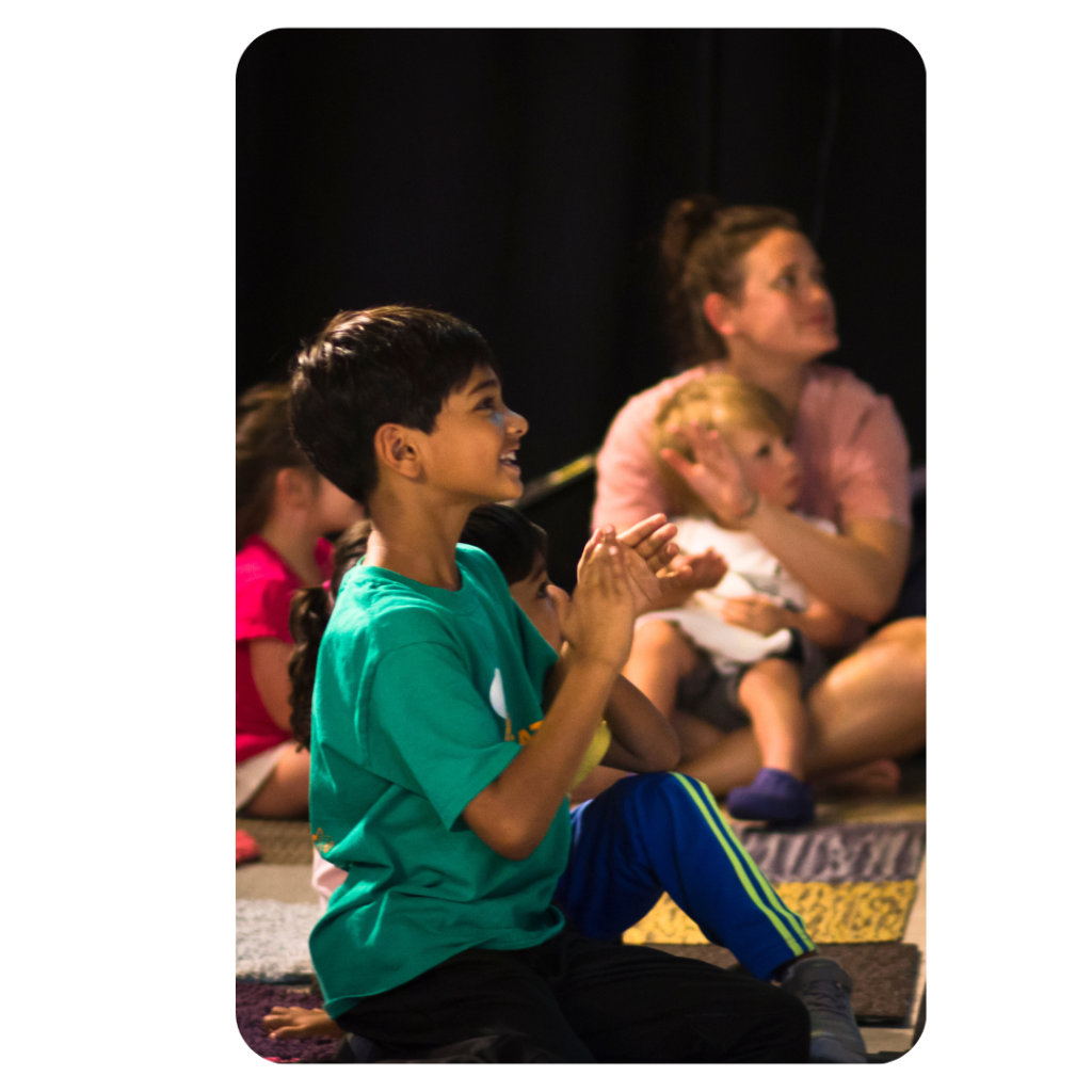 Young boy smiles and claps while sitting on floor.