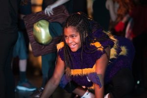 Child in a bumblebee costume leans forward while smiling.